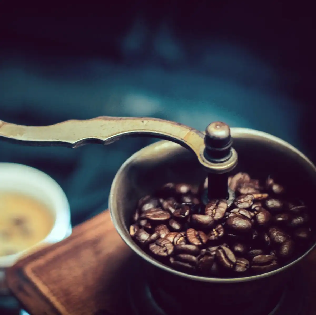 An old wooden box coffee grinder with a brass crank and a bowl of beans