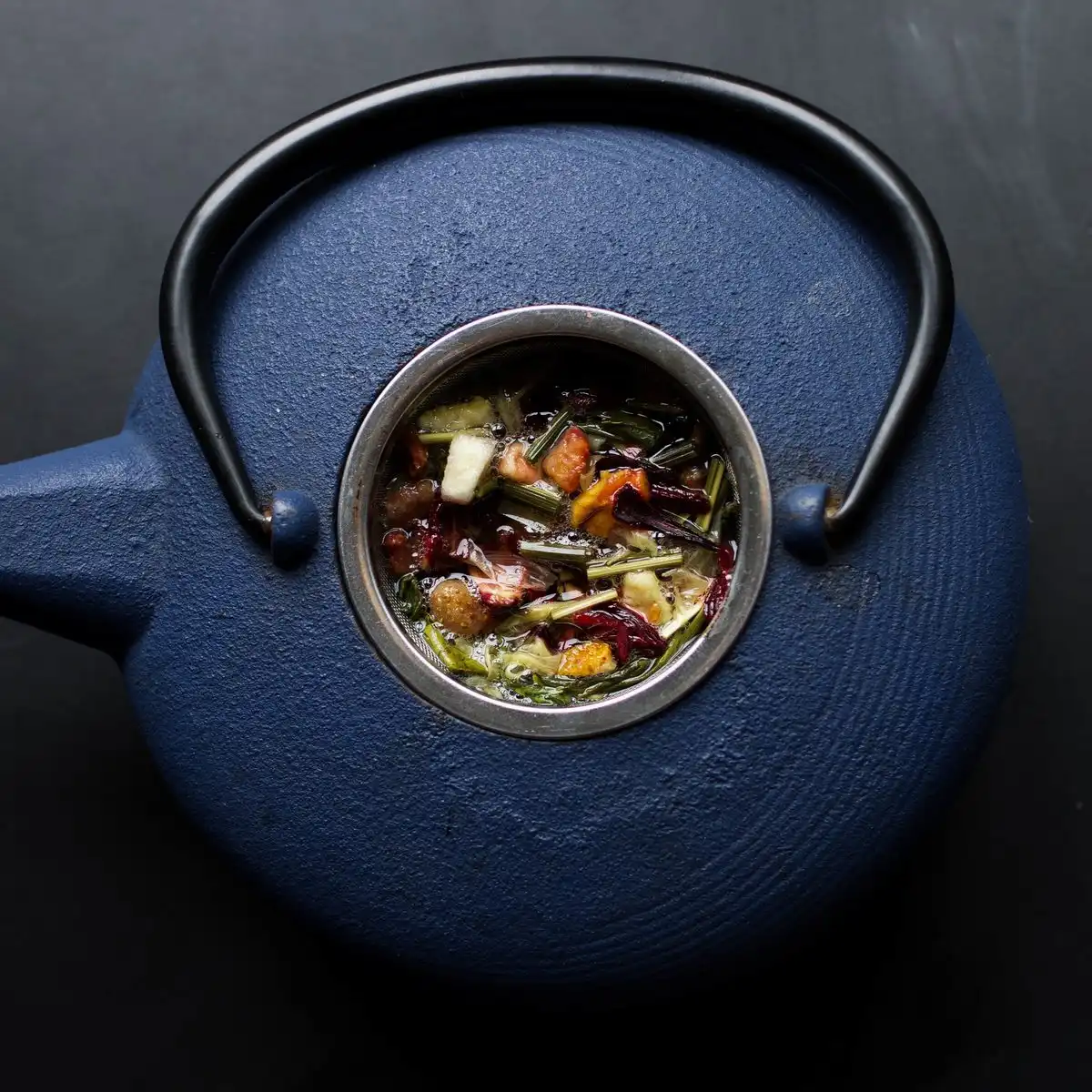 Loose black tea leaves in the strainer of a dark blue cast-iron teapot