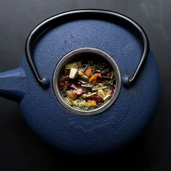 Loose black tea leaves in the strainer of a dark blue cast-iron teapot