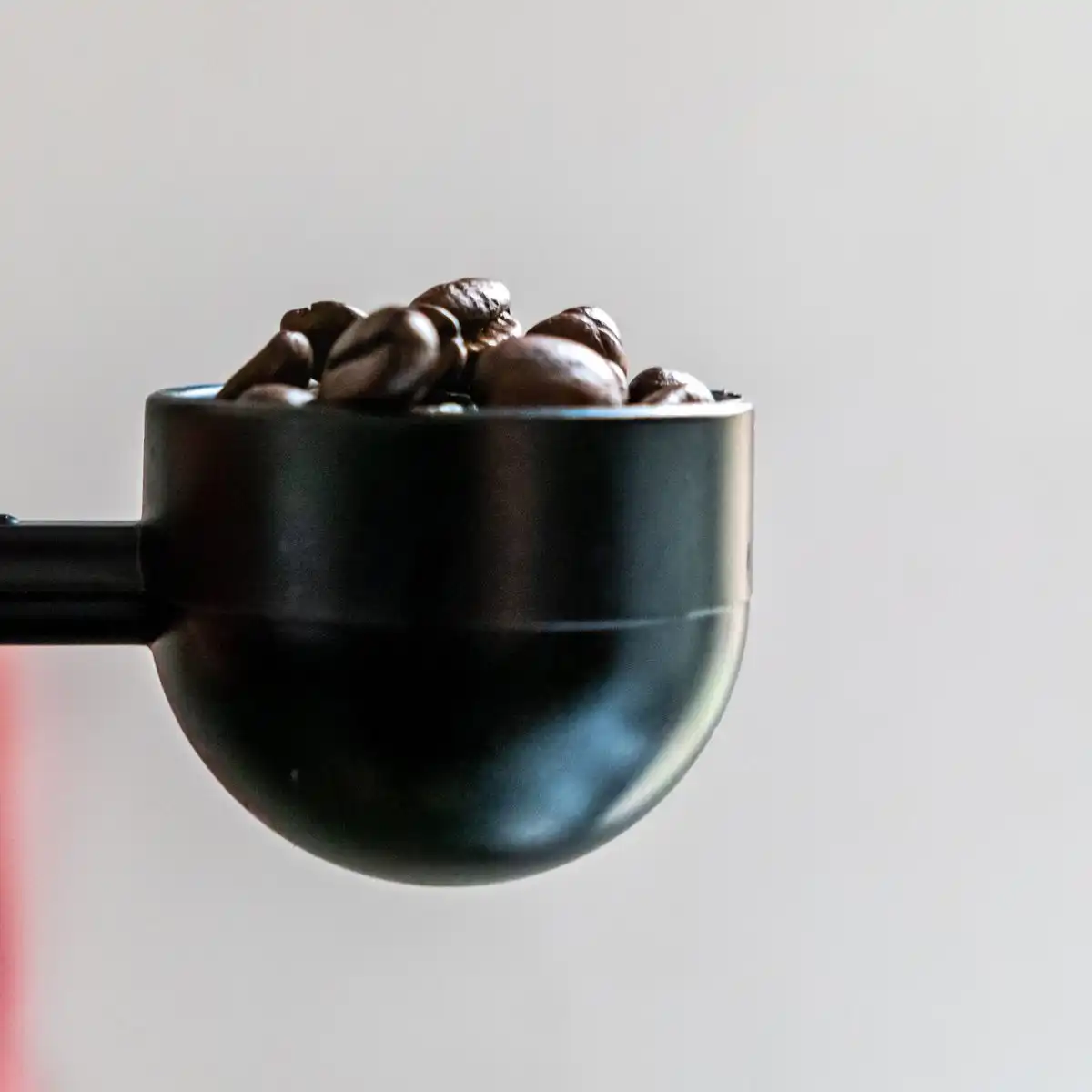 A black coffee scoop full of roasted beans held over a counter