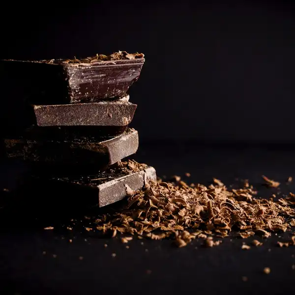 A stack of broken dark chocolate pieces with shavings on a black surface