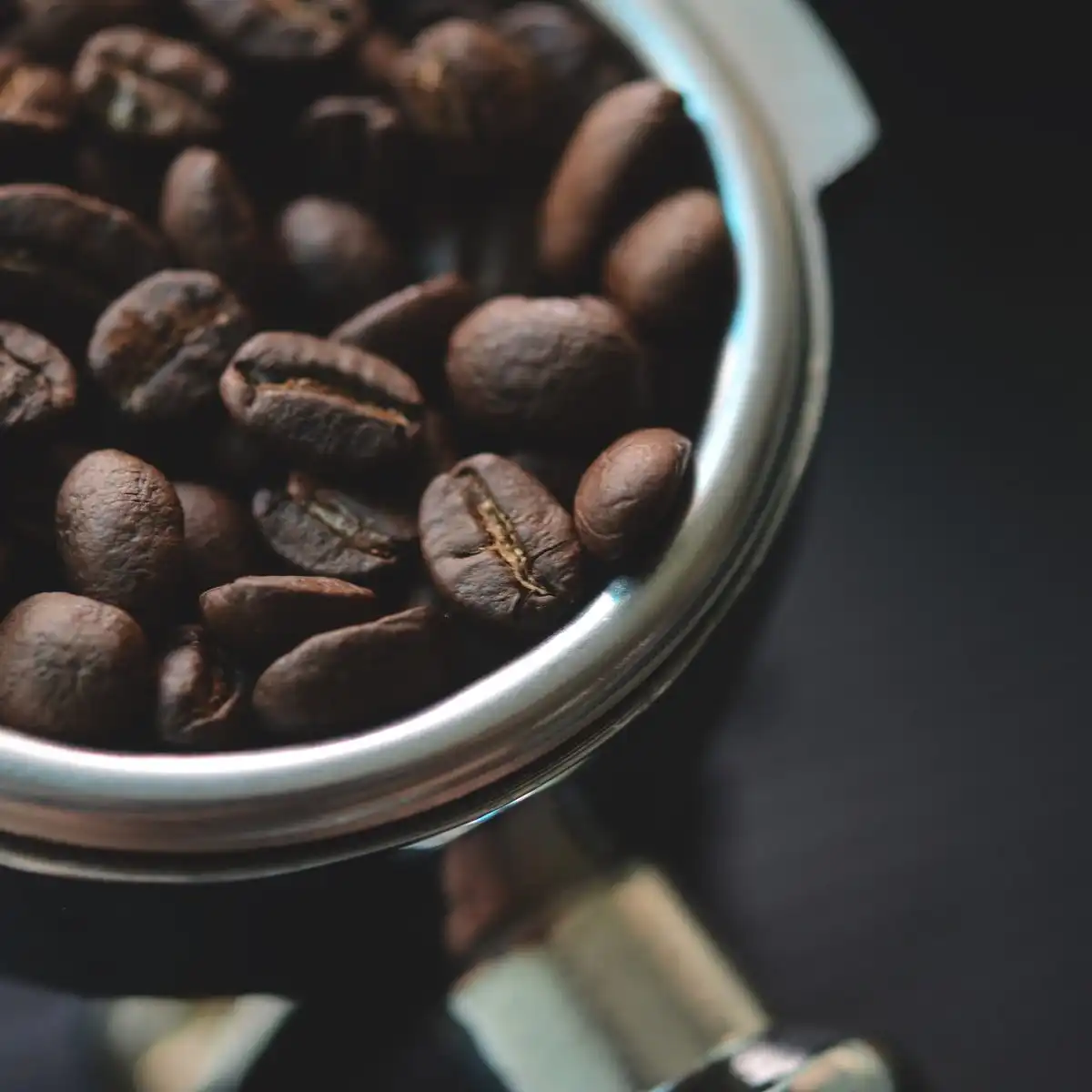 Dark roasted coffee beans piled in a steel espresso portafilter
