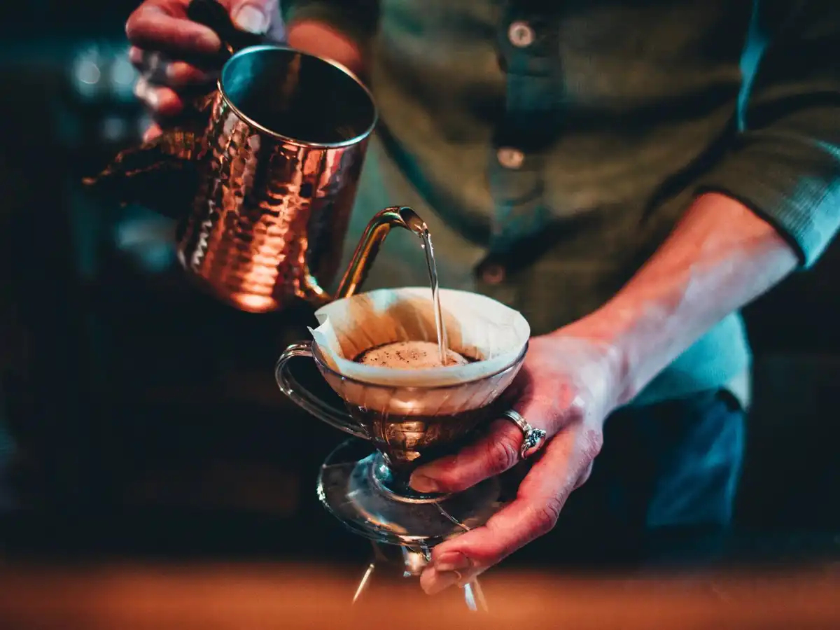 A person pouring hot water from a copper kettle into a pour-over brewer