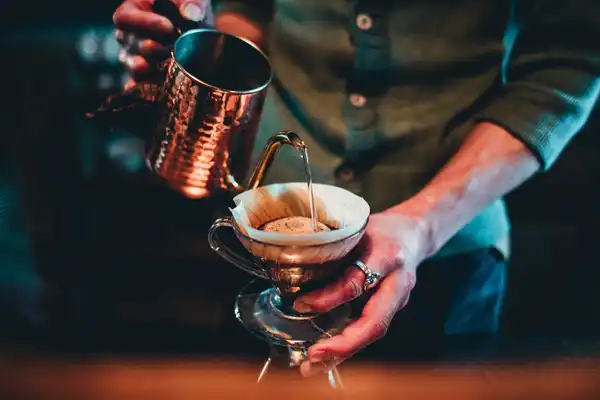 A person pouring hot water from a copper kettle into a pour-over brewer