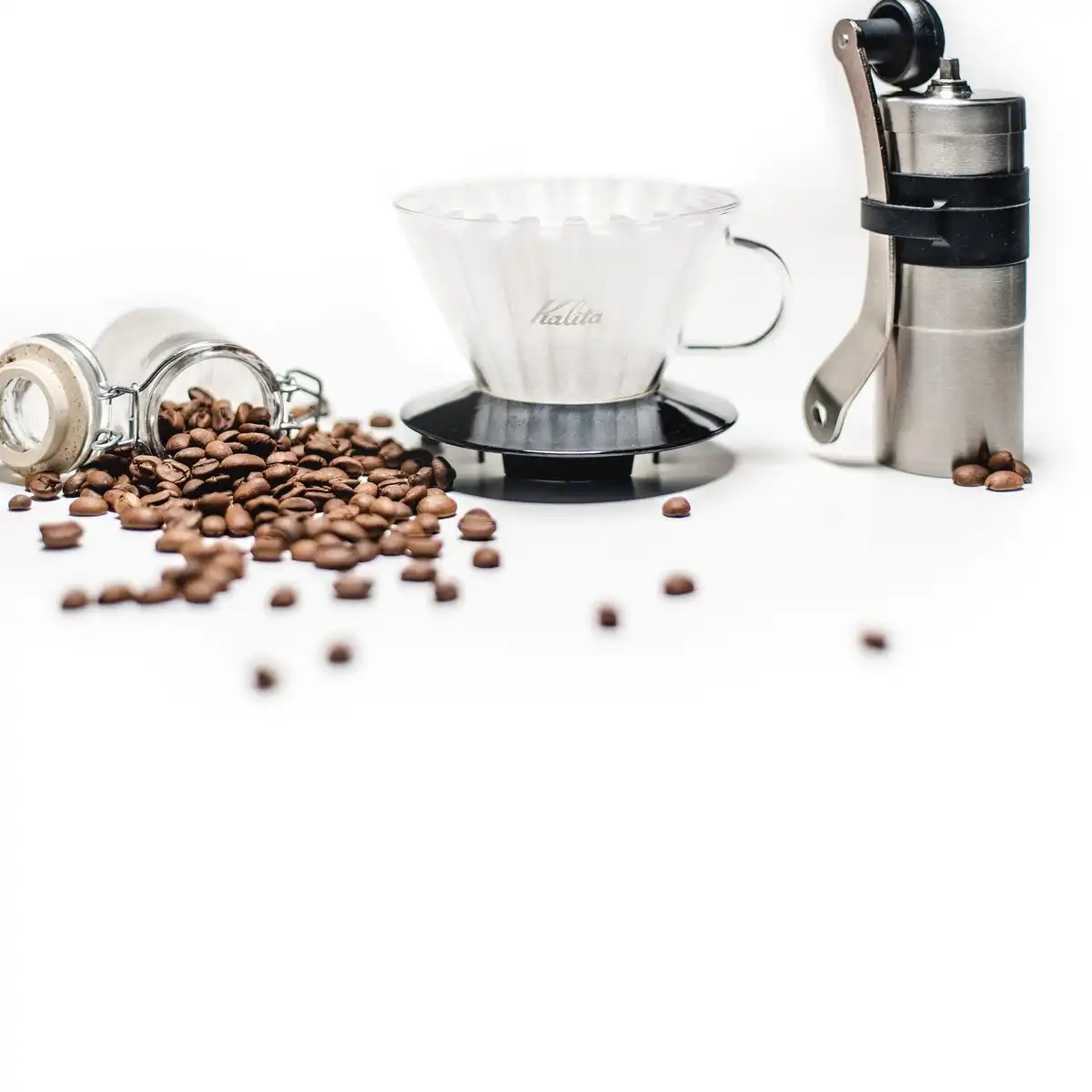 A white pour-over dripper on a stand beside a hand grinder and scattered coffee beans