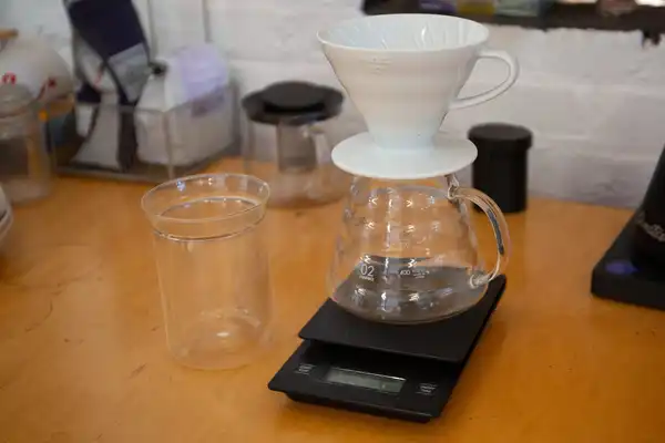 Two pour-over brewers, a glass server and a scale on a wooden counter