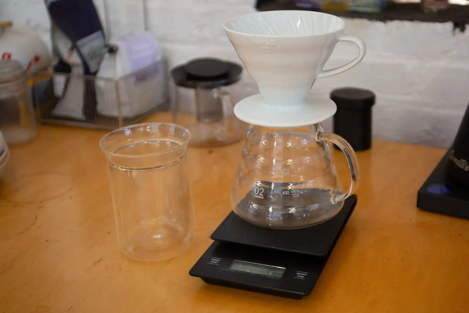 Two pour-over brewers, a glass server and a scale on a wooden counter