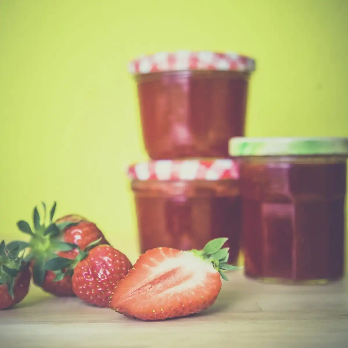 Two jars of red strawberry jam with fresh strawberries in front