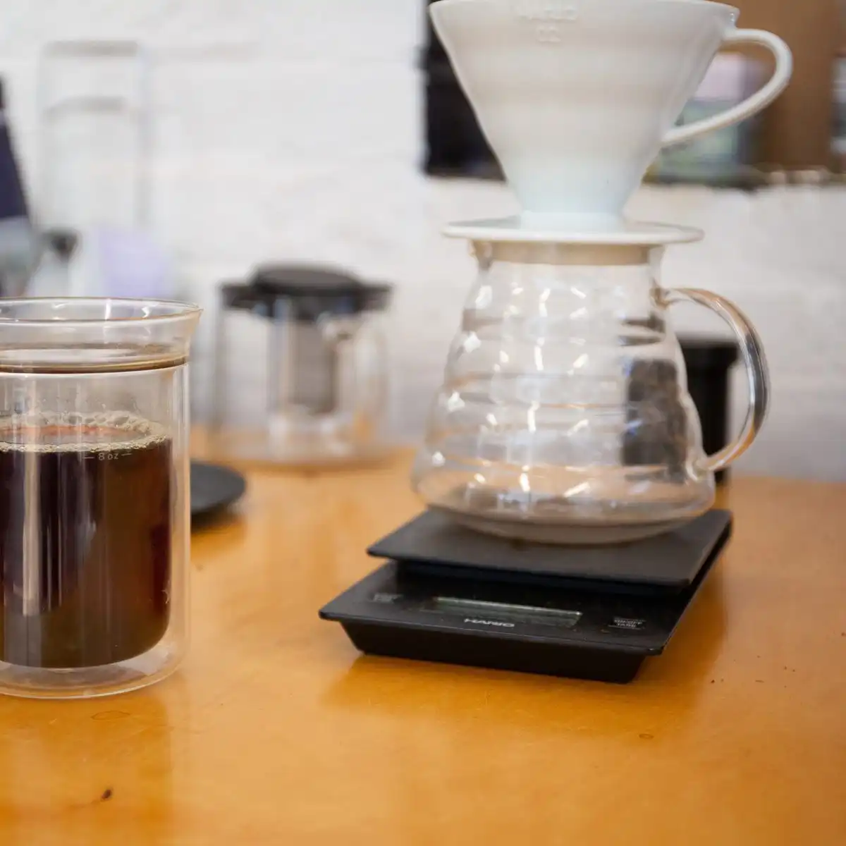 A glass pour-over brewer on a digital scale next to a cup of filter coffee